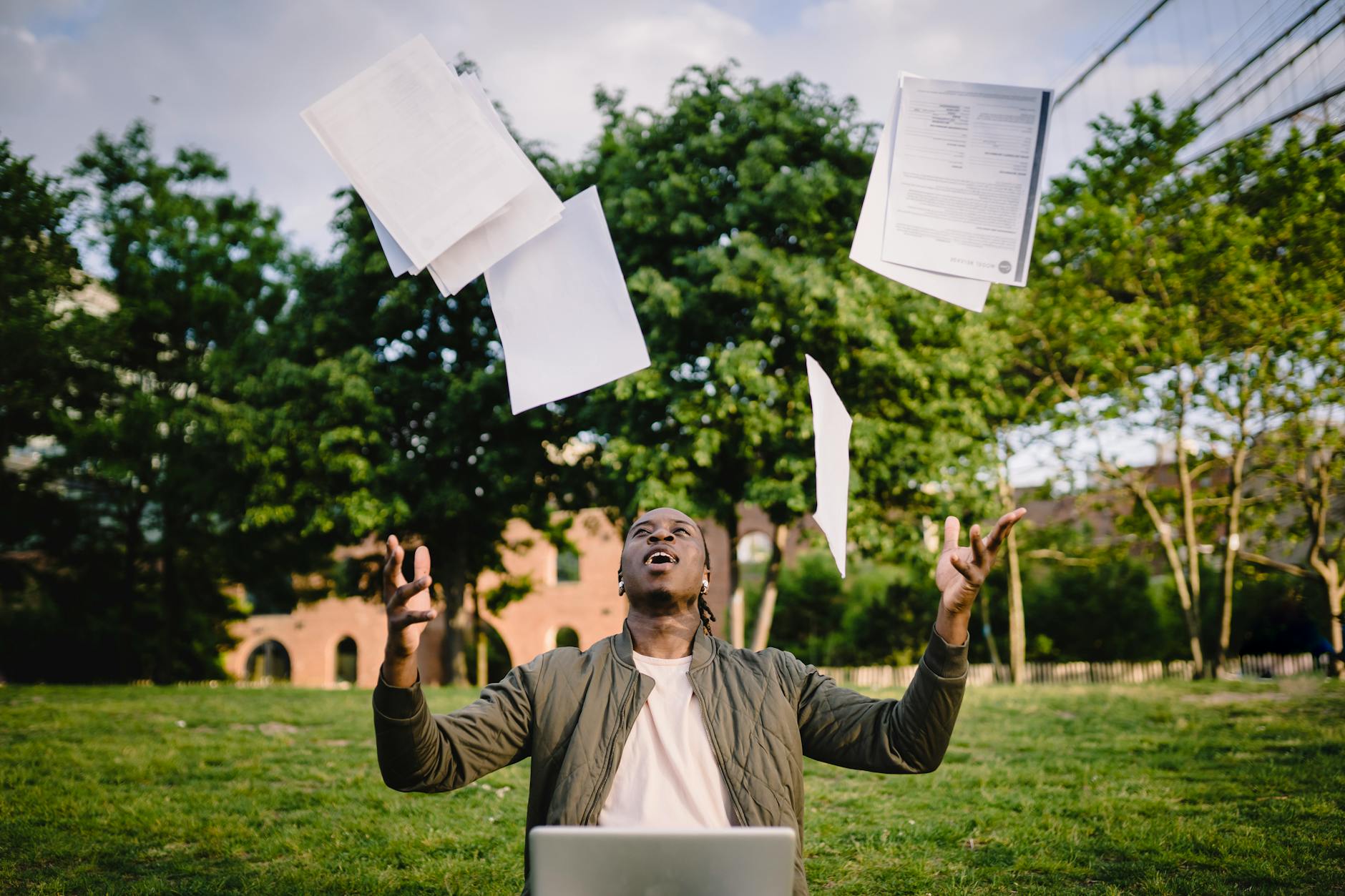 A frustrated man sits in front of a laptop, throwing resumes into the air in exasperation, symbolizing job search struggles and overlooked qualifications.
